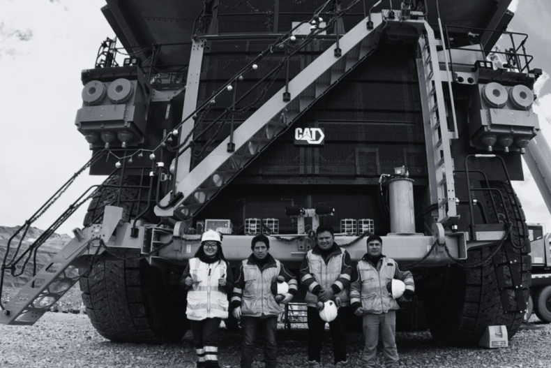 A black and white photo of a large CAT haul truck with four miners standing in front of it
